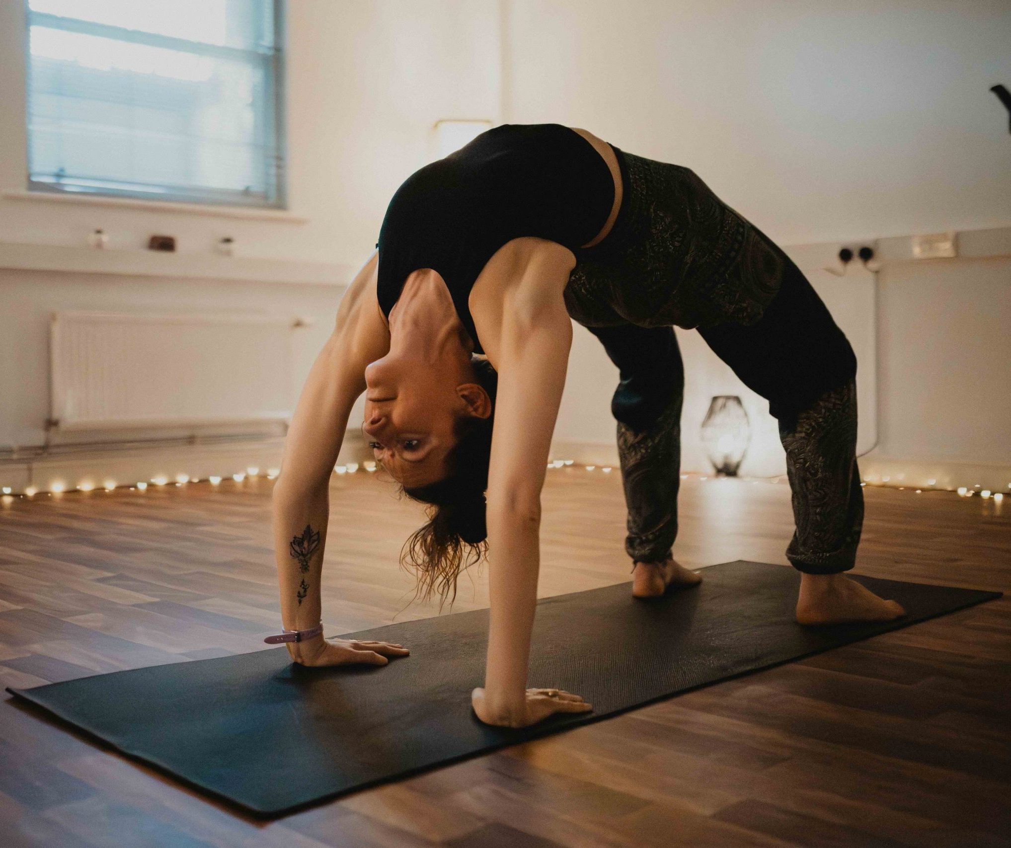 A white woman in black clothes doing a back bend in a yoga studio