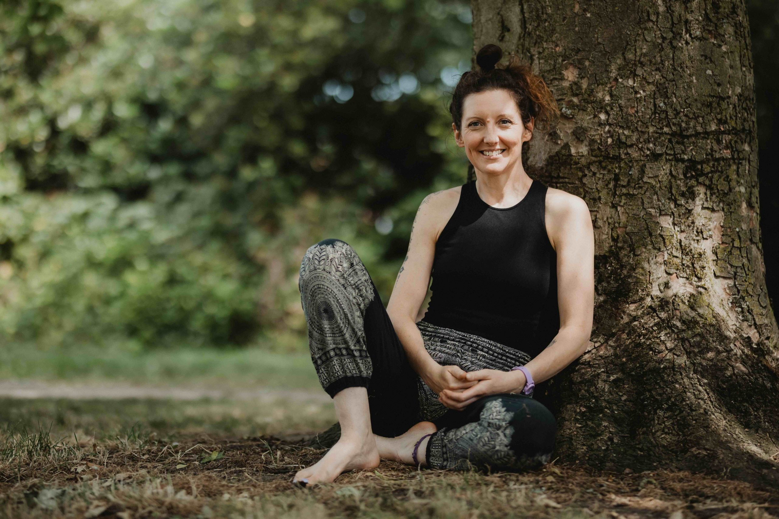 A woman in black clothing sat outside on the ground under a tree